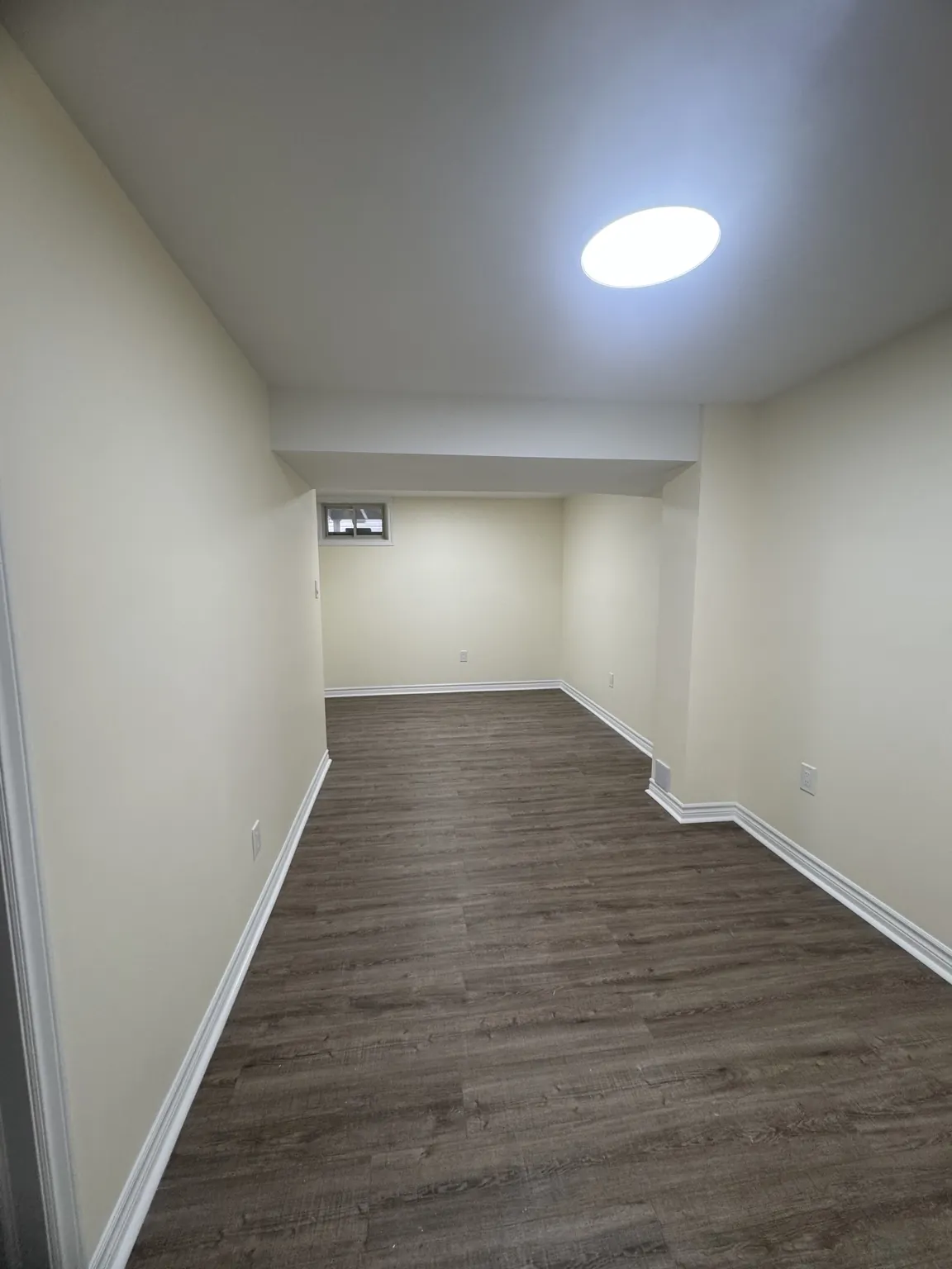 Finished basement room with clean white walls and plank flooring